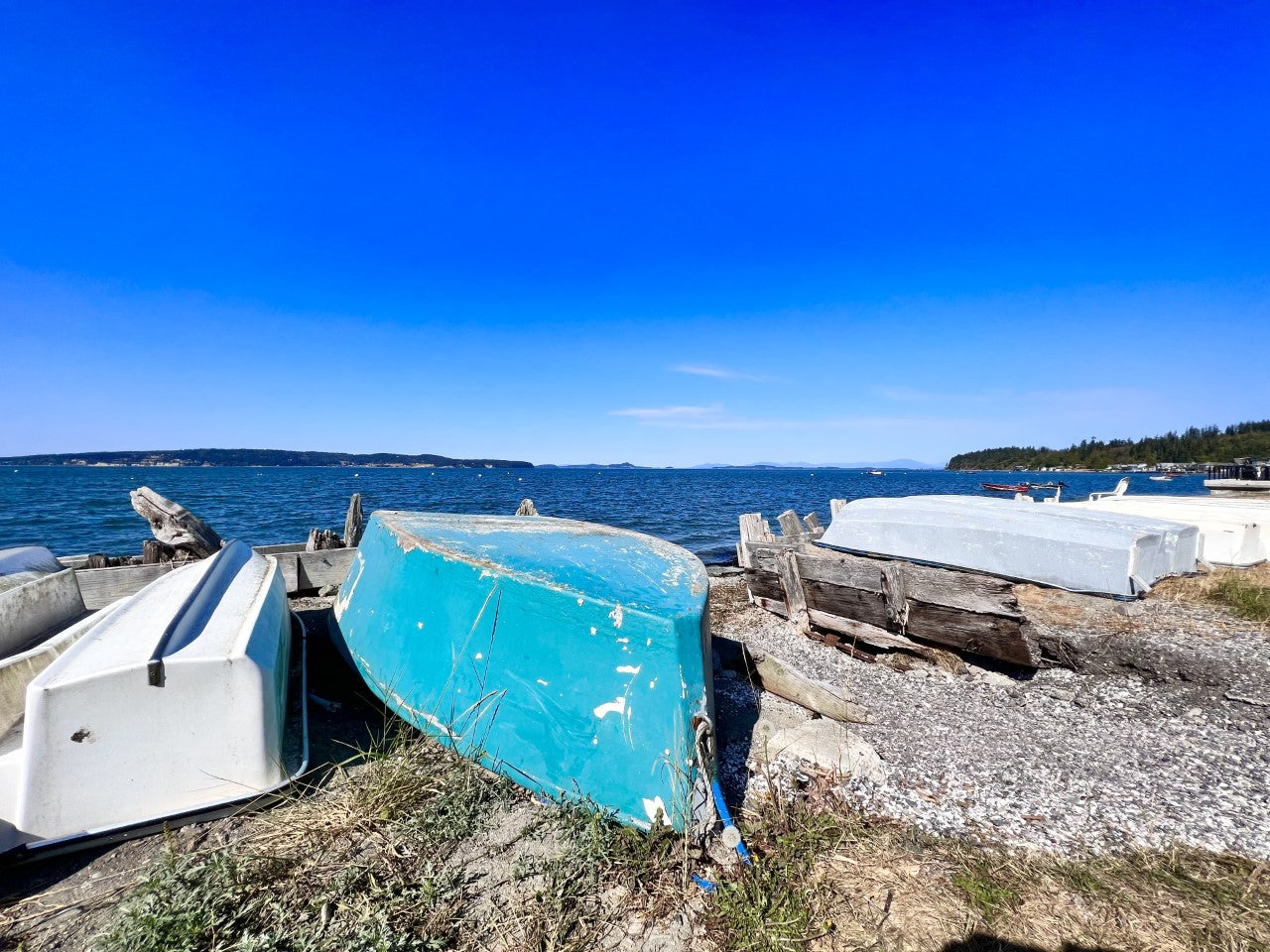 Boats on a rocky shore with clear blue water and sky.